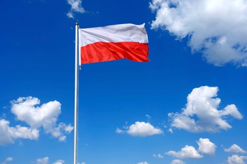 The flag of Poland flutters in the wind in a blue sky with white clouds