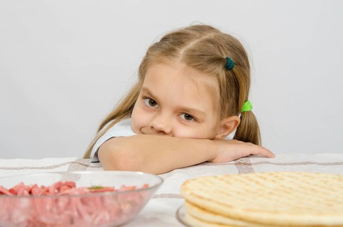 Little girl sitting at a table with his head on his hand with a smile and looking at the food in