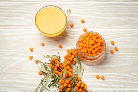 Sea buckthorn healthy hot tea in transparent glass cup, ripe berries in glass jar and branches with