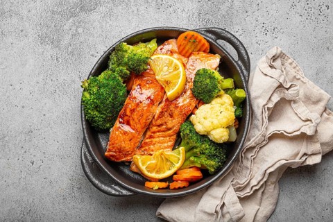 Healthy baked fish salmon steaks, broccoli, cauliflower, carrot in black cast iron casserole bowl