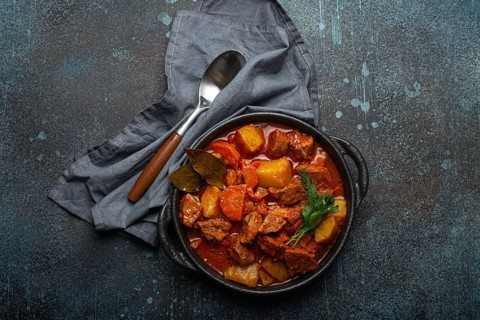 Beef meat stew with potatoes, carrot and delicious gravy in black casserole pot with bay leaves and