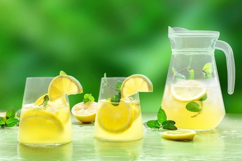 Lemonade with mint on a green background. Lemon water drink with ice. Two glasses and a pitcher.