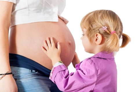 Daughter hugging mother's pregnant belly isolated on white