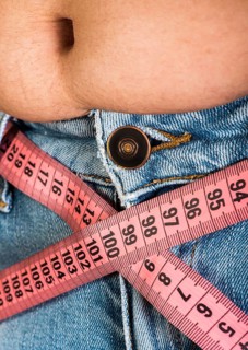 Woman showing fat belly. Pink tape measure
