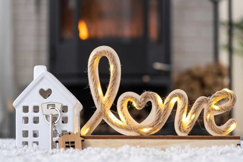 Key to house with keychain against background of fireplace stove with fire and firewood in