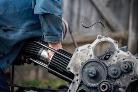 A person working on an engine outdoors, focusing on metal and mechanical components