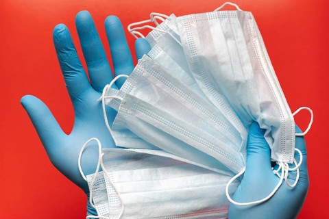 Doctor holds respiratory surgical face mask in hands blue medical gloves on red background.