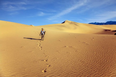 Woman with a camera and a tripod goes among the dunes. USA. Mesquite Flat Sand Dunes, Death Valley,