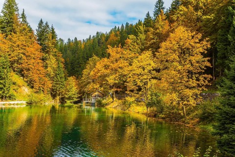 Fantastically beautiful autumn forests are reflected in the quiet lake Lago de Fusine. Easy ripples