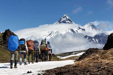 Group of hikers climbing in Kamchatka mountain on background of Klyuchevskaya group of volcanoes: