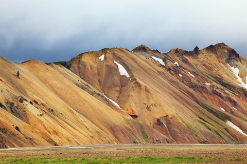 Smooth orange rhyolite mountains in Landmannalaugar nature reserve. In the hollows snow left over