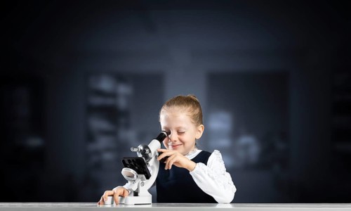 Little girl scientist looking through microscope in classroom at biology lesson. Research and