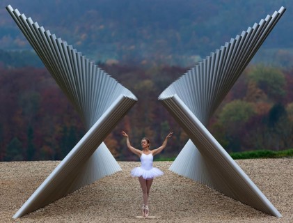 Ballerina in white ballet costume in elegant pose in front of modern sculpture in autumnal