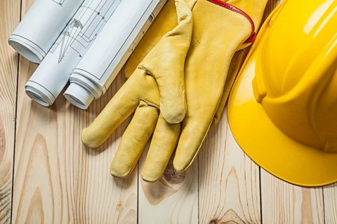 Blueprints yellow gloves and construction helmet on wood boards
