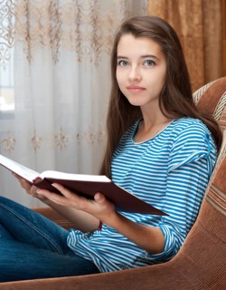 A young caucasian teenage girl reads a book sitting in an armchair