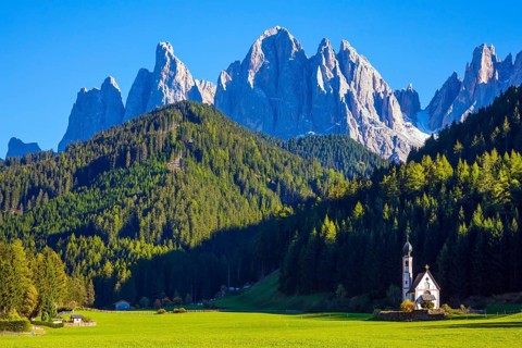 Small white church with among green lawns on the sunset. The village Santa Maddalena in the Val di