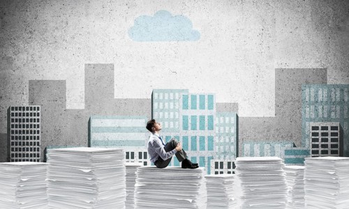 Thoughtful businessman looking away while sitting on pile of documents with drawn cityscape on