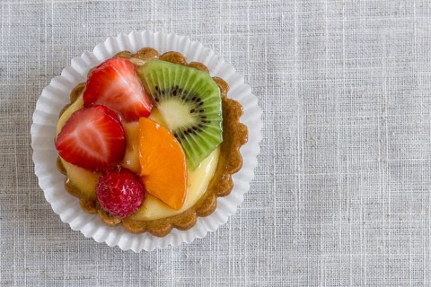 A cake with cream and mixed fruit, resting on linen tablecloth
