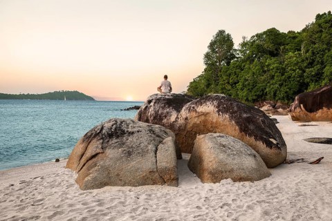 Young Man Meditating and doing Yoga Exercises against beautiful ocean view on stones