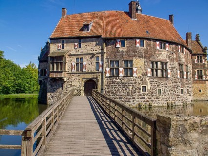 Historic castle with striking wooden bridge and tiled roof, surrounded by moat and blue sky,