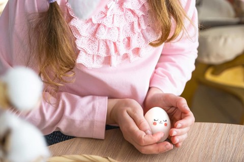 A cute girl with pink bunny ears makes an Easter craft, decorates an egg in the form of a unicorn