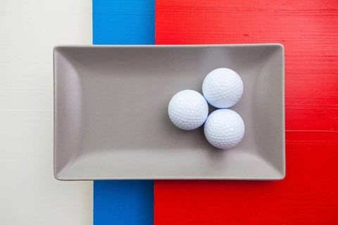 Gray ceramic dish with golf equipments on over white, blue and red wooden table, rectangle dish
