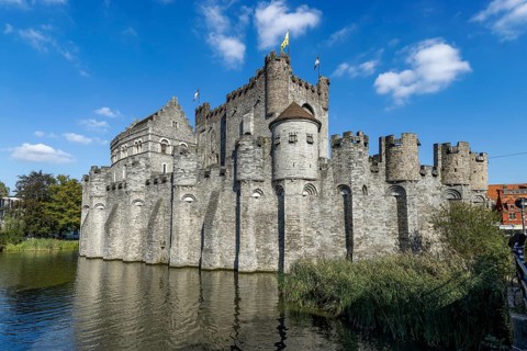 Stone walls of medieval Gravensteen Castle and moat with blue sky, Ghent, East Flanders, Belgium