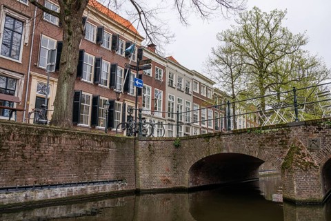 A canal with a stone bridge and historic buildings in the background, bicycles next to the bridge,