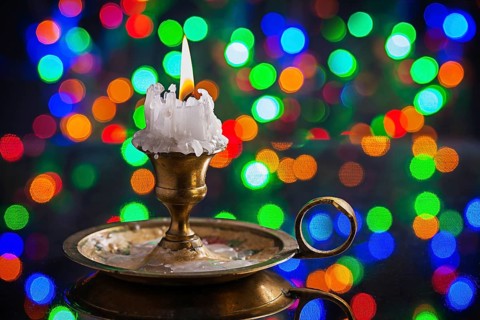 Glowing old candle in wintage candlestick on surface of mirror with multycolored bokeh horizontal