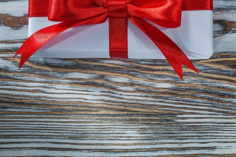 Red present box with ribbon on wooden background