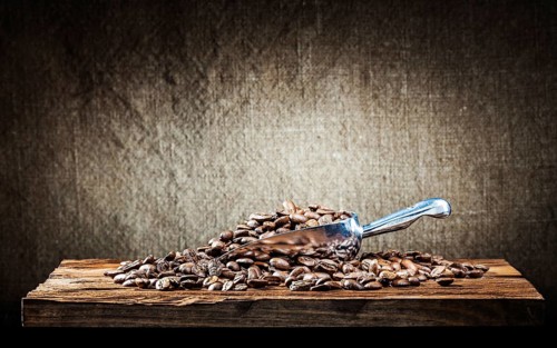 Metallic scoop with coffee beans on vintage wood