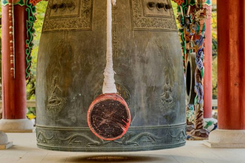 Closeup of bronze bell and striker in pavilion in mountainside Buddhist temple