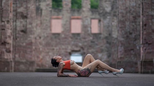 Woman in sporty pose and high heels lying on the ground in front of an old ruin, Staged outdoor