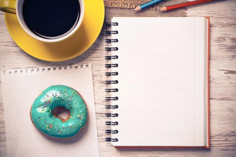 Opened notepad and cup of coffee with donut on wooden table