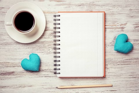 Coffee cup notepad pencil and two hearts on wooden surface
