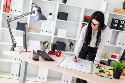 A young girl with glasses, wearing a white blouse and black trousers, works in the office. The girl
