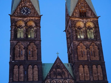 Detailed view of two Gothic church towers with clocks, illuminated in the soft evening mood,