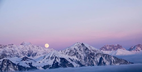 full moon rising into a pink sky in a winter mountain landscape in the Alps of Switzerland