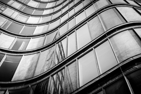 Curved building with shiny windows with reflections in black and white tone