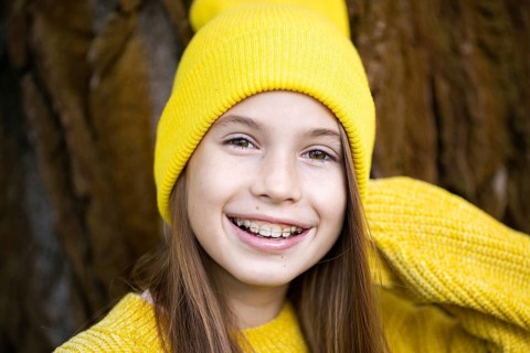 Cute and happy teenage girl with braces smiling at camera in yellow clothes in park. Concept of