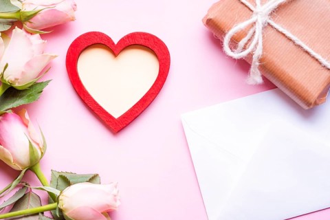 Valentine day theme image with a red heart with copy space in the middle, surrounded by pink roses,