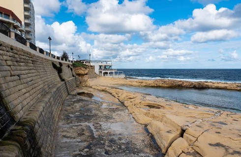 Saint Julian, Malta, 01 07 2022: Low angle view over the water, rocks and sand at the beach with