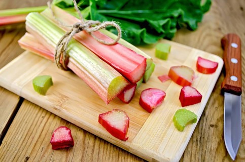Bundle of stalks rhubarb, cut pieces of rhubarb with a sheet and a knife on a wooden boards