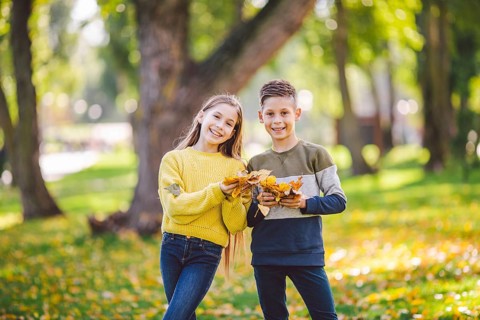 Happy Caucasian siblings enjoying in autumn day in park, sunny weather. Kids having fun holding