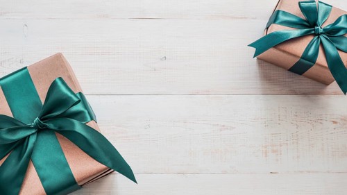 Two gift boxes in craft wrapping paper and green satin ribbon on white wooden table, copy space in