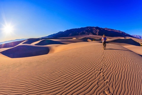Woman - photographer is among the gently sloping sand dunes. Sunrise in the orange sands of the