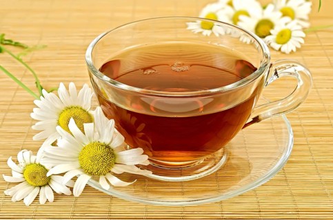 Herbal tea in a glass cup with saucer, camomile on a background of bamboo napkins