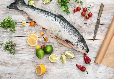 Raw salmon fish in ice and vegetables on white table. Baking paper