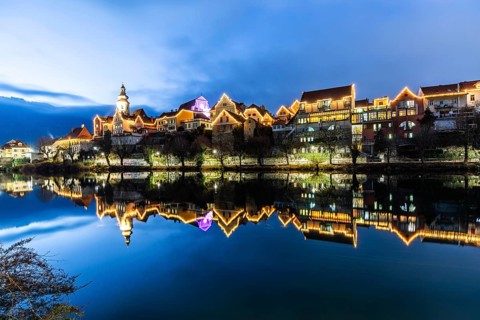 Christmas illuminated house facade of Frohnleiten reflected in the river Mur, blue hour,