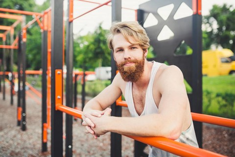 Portrait young bearded man standing on public sports ground and training on parallel bars. Handsome